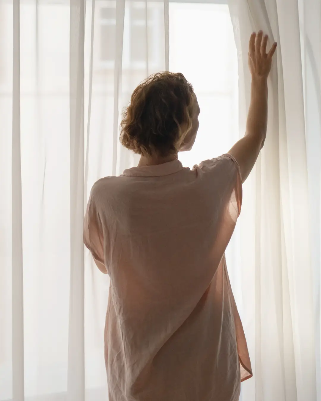 woman gently pushing curtains aside of window